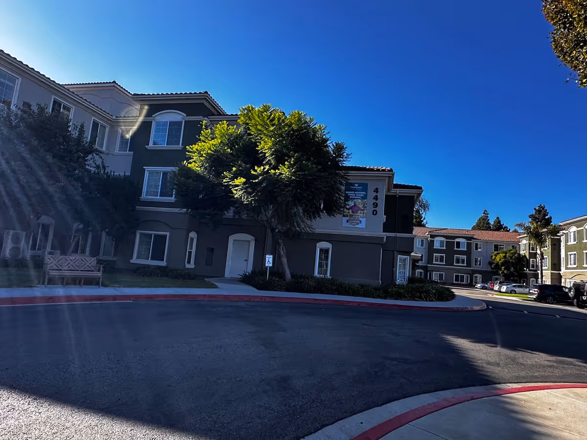 Front exterior of a multi-story senior living building with trees, a driveway and visible address number 4490.