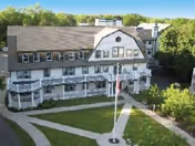 A white, multi-story senior living facility with gray roof, flagpole, and surrounding green lawn.