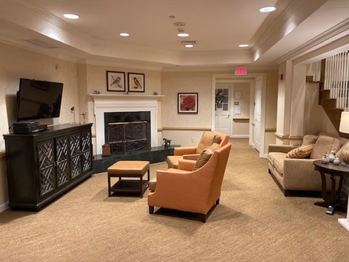 Cozy common lounge with armchairs, a sofa, TV console and fireplace in a senior living facility.