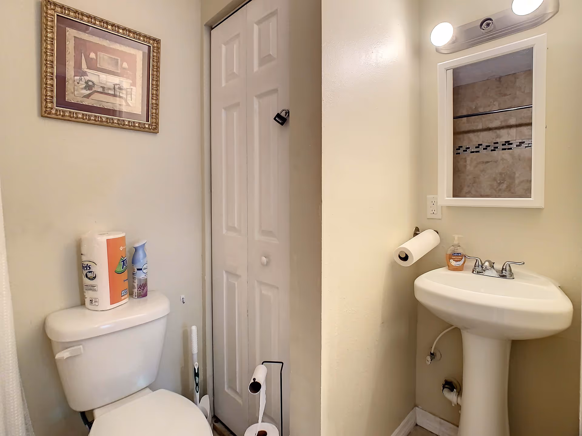 Small bathroom with a toilet, pedestal sink, mirror, and a bi-fold closet door.