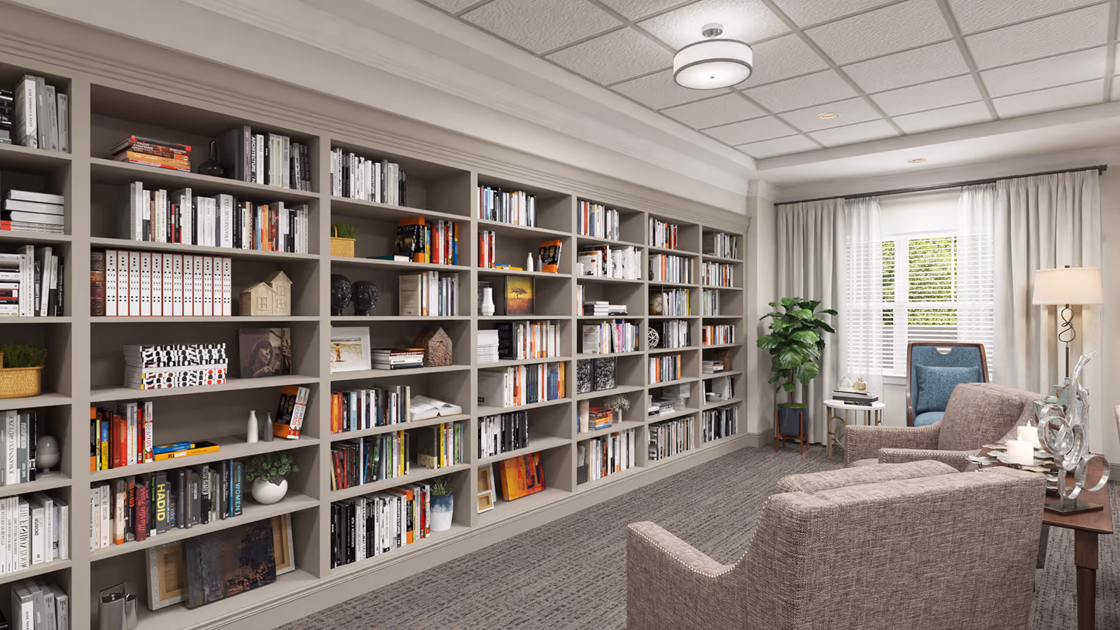 A cozy library or reading room with a large built-in bookshelf filled with books and decorative items. There are two upholstered armchairs and a side table with candles and a decorative sculpture. A window with white blinds and light curtains allows natural light into the room, and a floor lamp stands nearby. The ceiling has a modern light fixture and a grid pattern.