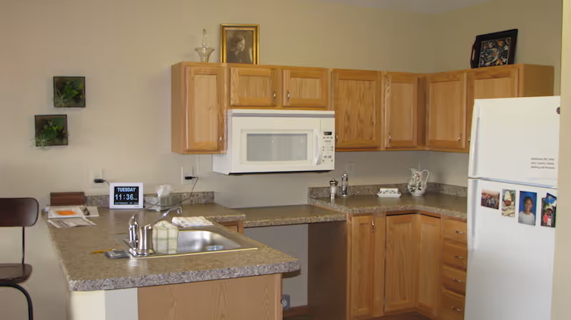 Small kitchen with oak cabinets, a microwave over the counter, an island sink, and a refrigerator with photos.