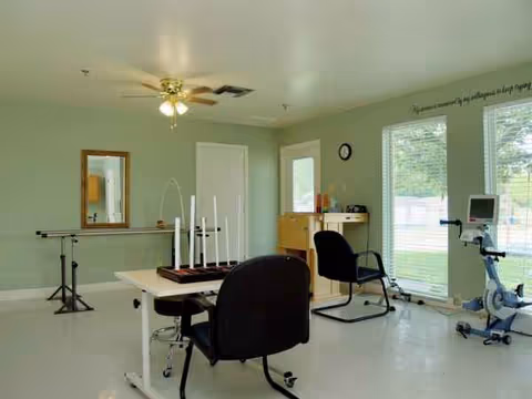 Light green interior room with chairs, a desk, mirror, ceiling fan, and exercise equipment.