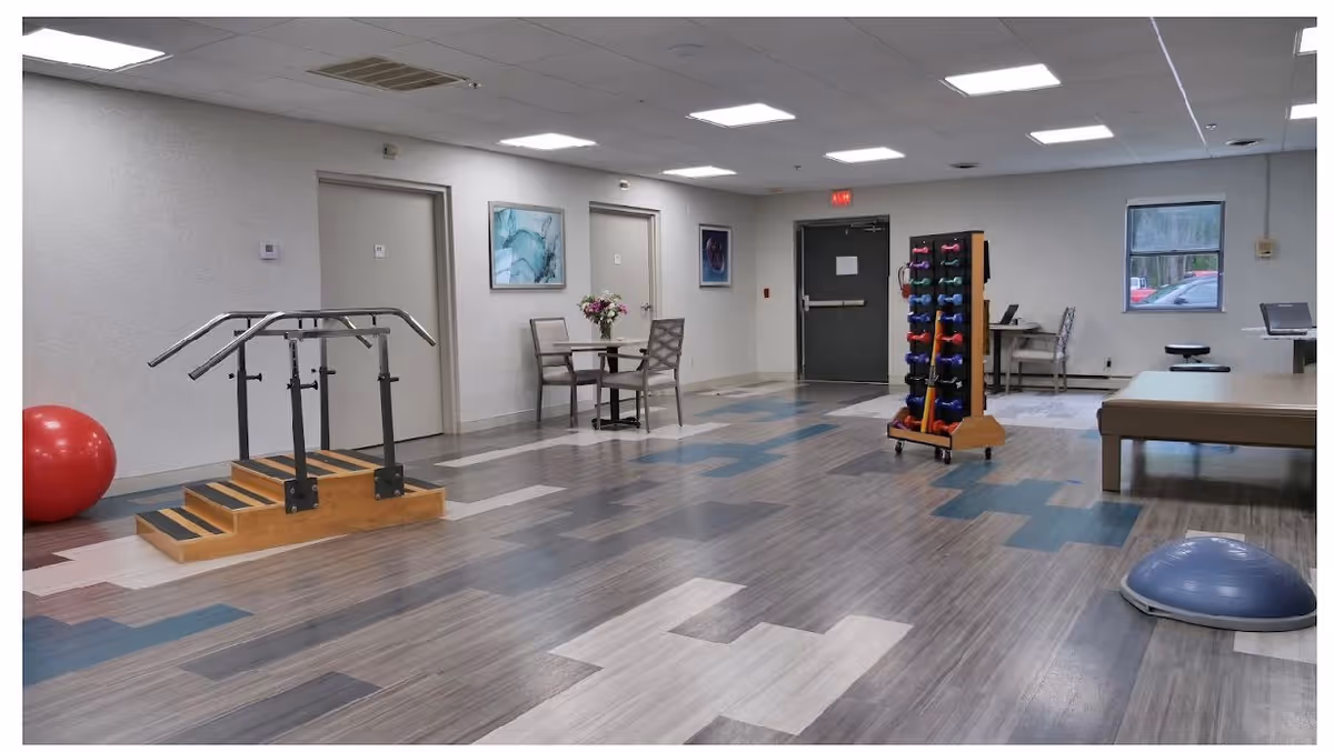 Rehabilitation therapy room with parallel bars, exercise equipment, dumbbells, and a therapy table.