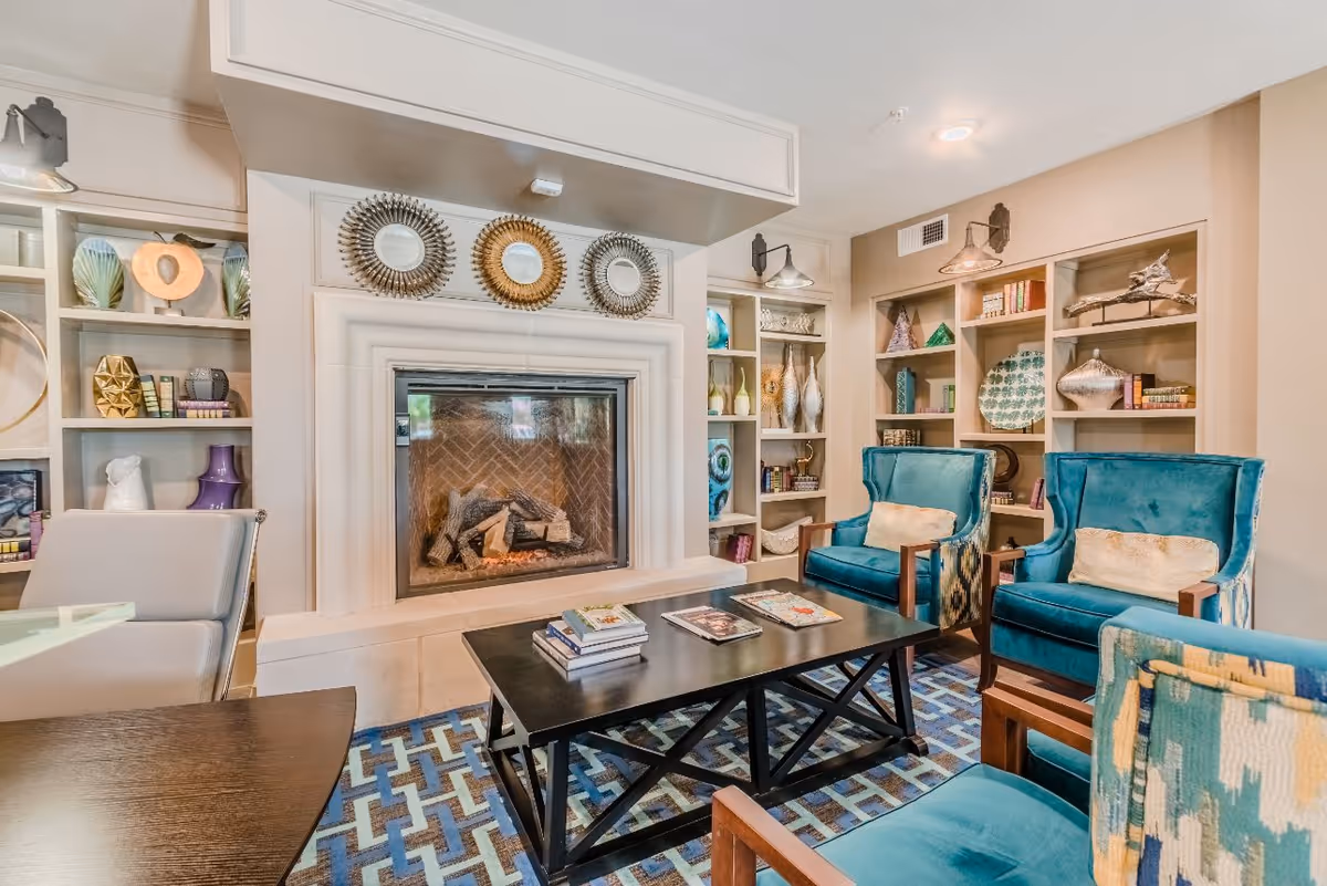 Cozy communal living room with a fireplace, built-in shelving, a central coffee table and teal armchairs.
