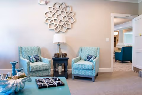 Two turquoise chairs flank a dark side table with a lamp in a cozy living area.