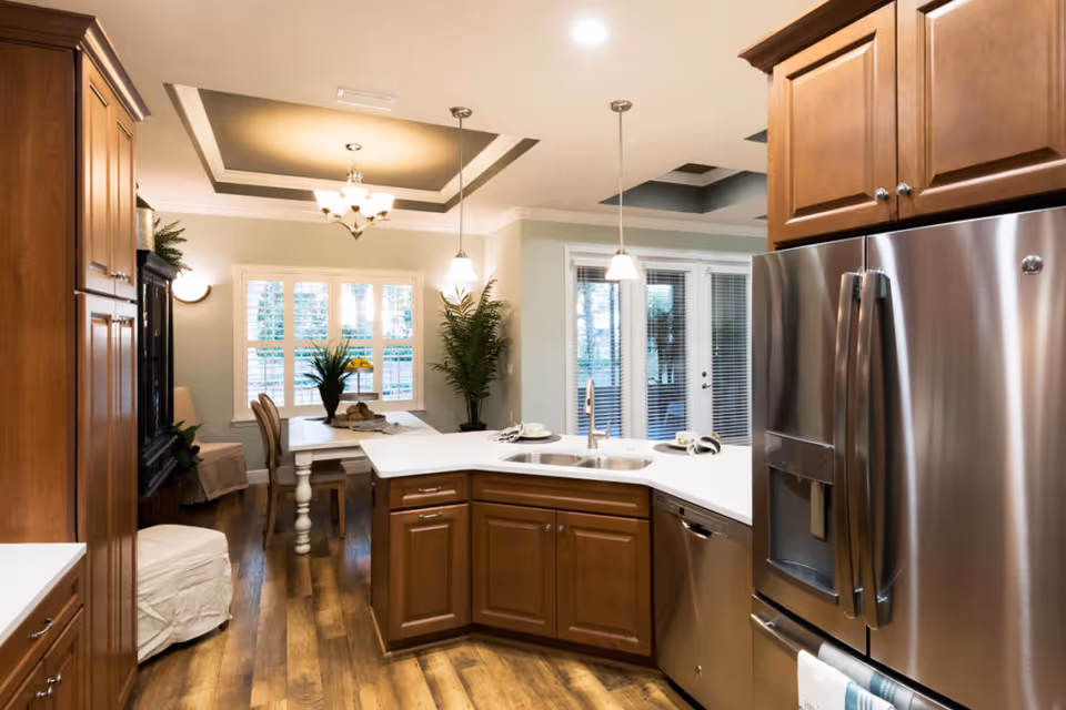 Open-concept kitchen with wooden cabinets, a center island with a sink, stainless steel refrigerator, and a dining area by windows.