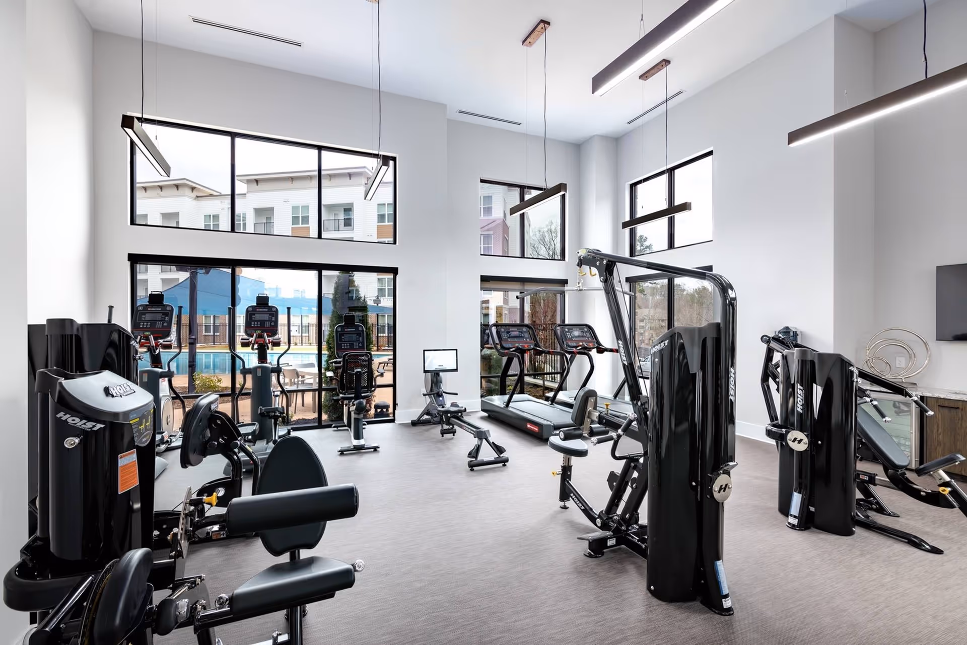 Bright fitness center with treadmills, weight machines, and large windows overlooking an outdoor pool area.