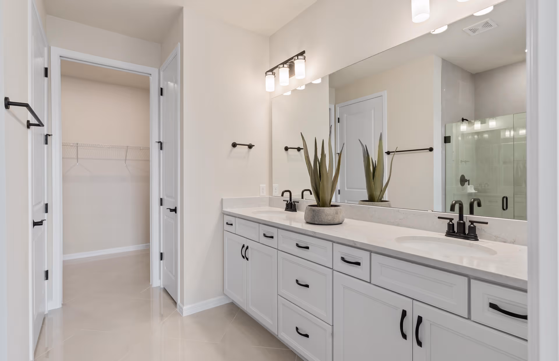 Bright modern bathroom with a double-sink vanity, large mirror, walk-in closet doorway and glass shower.