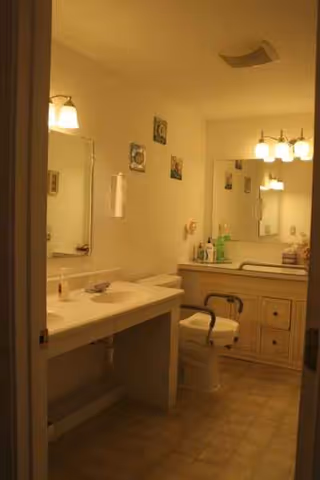 Dimly lit communal bathroom with double sink vanity, mirrors, and a toilet.