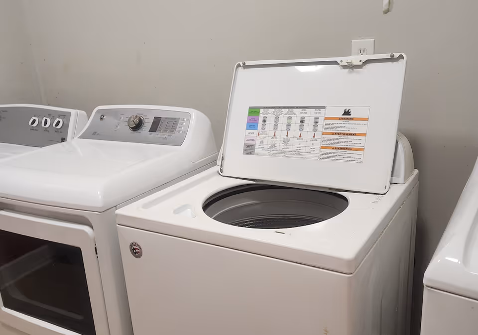 Top-loading washing machine with its lid open next to a dryer in a small laundry room.