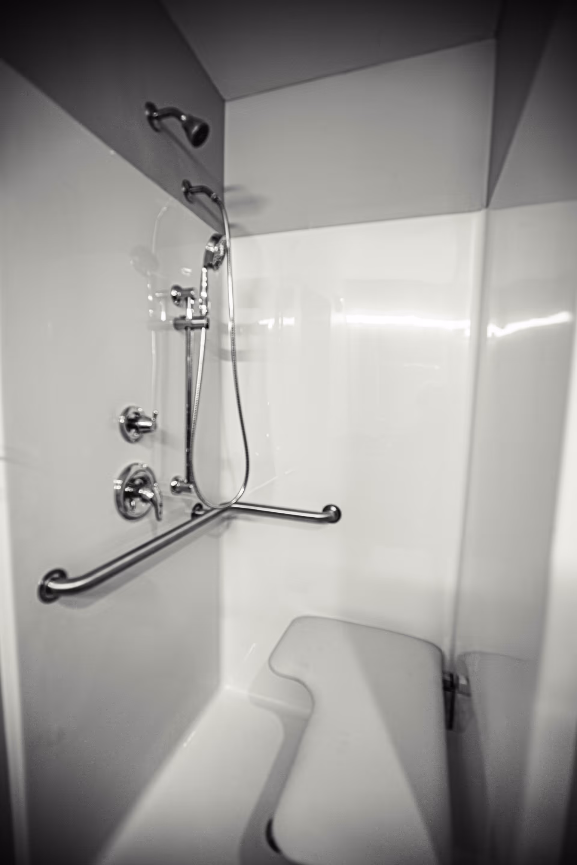A white shower stall with a built-in bench seat, a handheld showerhead, and a horizontal grab bar for support.