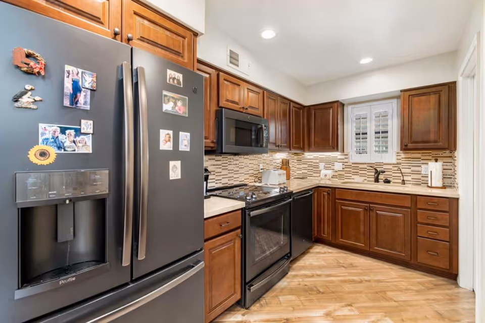 Bright kitchen with dark wood cabinets, a double-door black refrigerator, black stove and microwave, and a patterned tile backsplash.