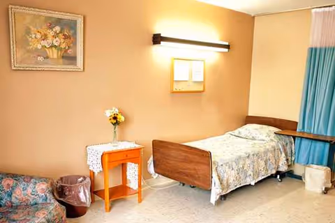 A single patient bedroom featuring a bed, nightstand, floral painting, and a blue curtain.