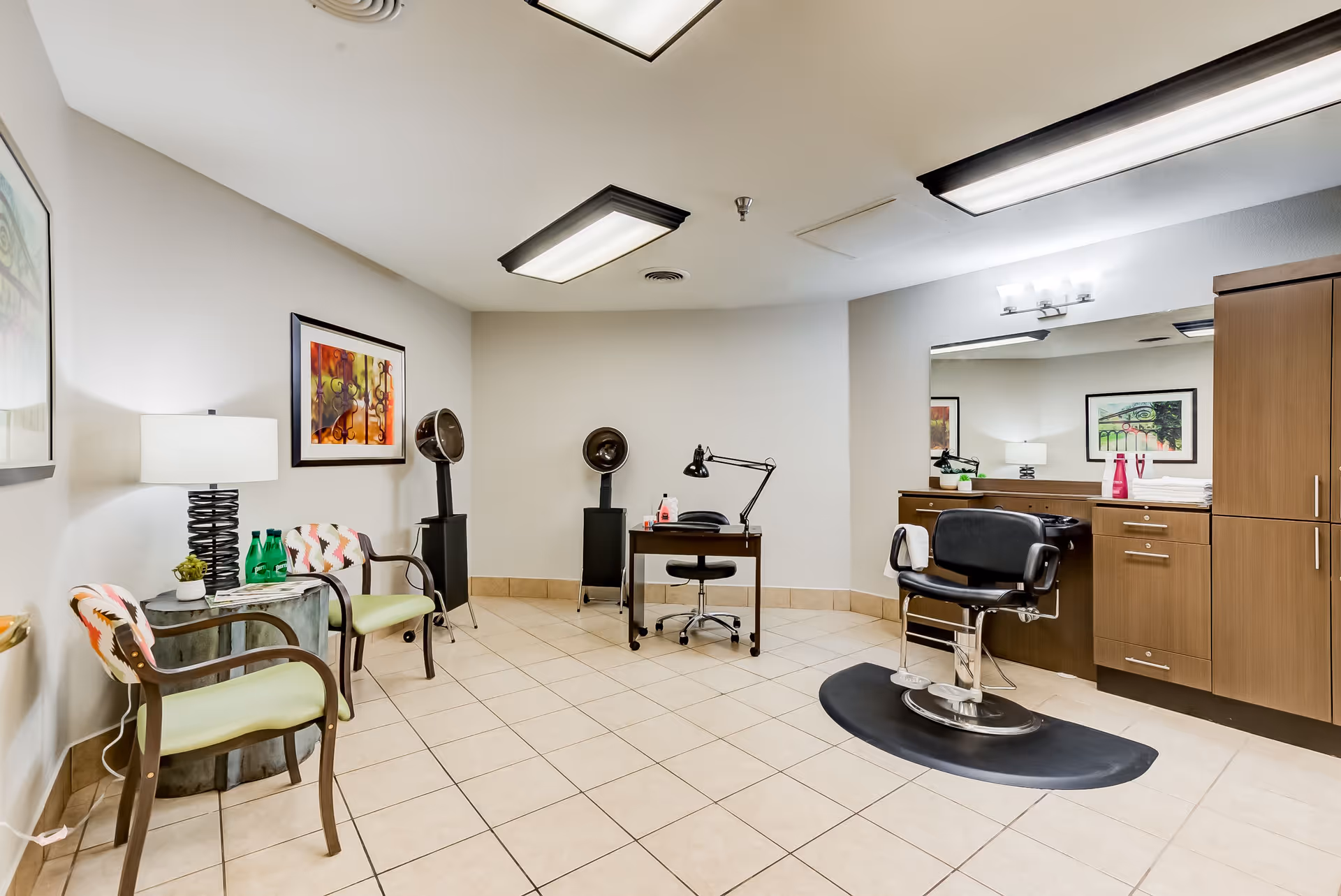 Bright salon/hair-styling room with a styling chair, hooded dryers, waiting chairs, a desk and cabinetry.