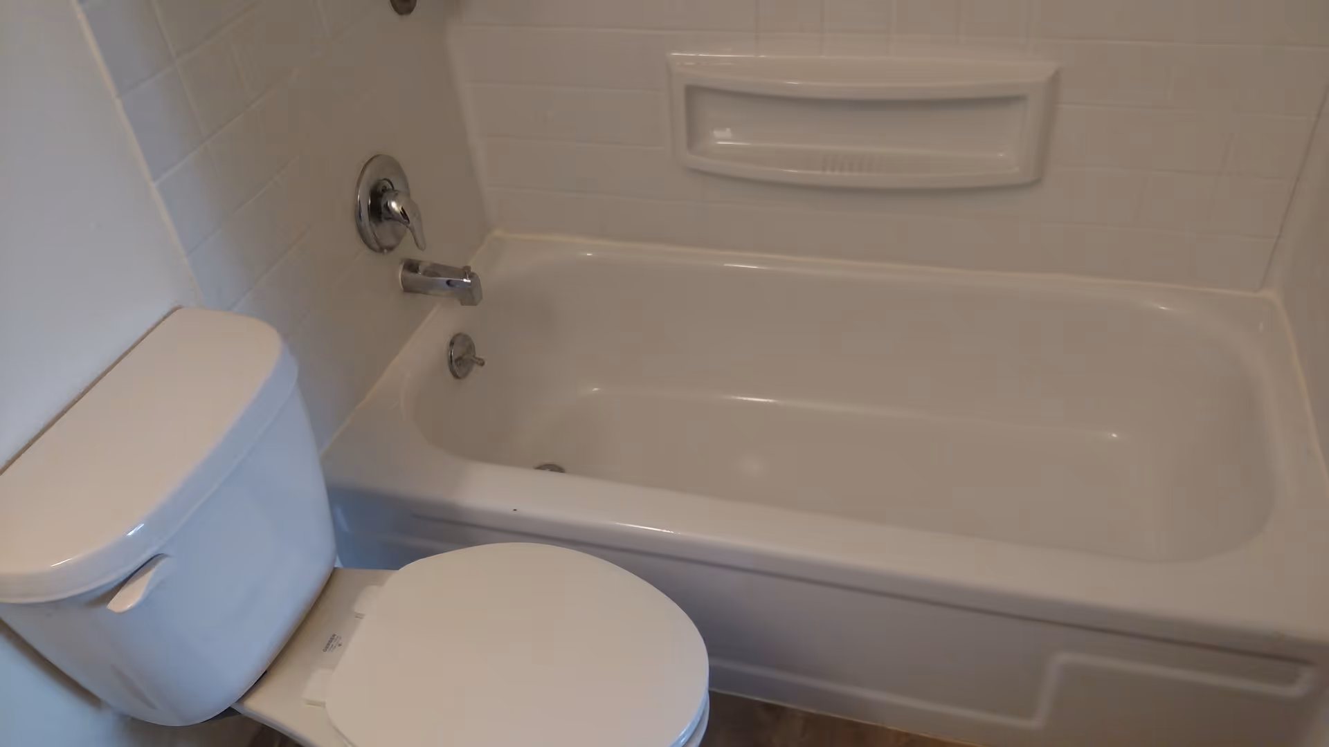 A clean bathroom featuring a white bathtub with a built-in soap holder and chrome faucet fixtures, alongside a white toilet with the lid closed.