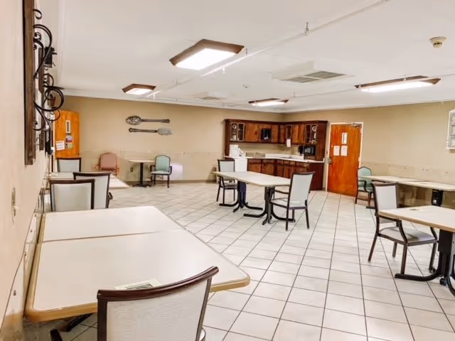 Spacious communal dining room with several tables and chairs and a small kitchenette along the back wall.