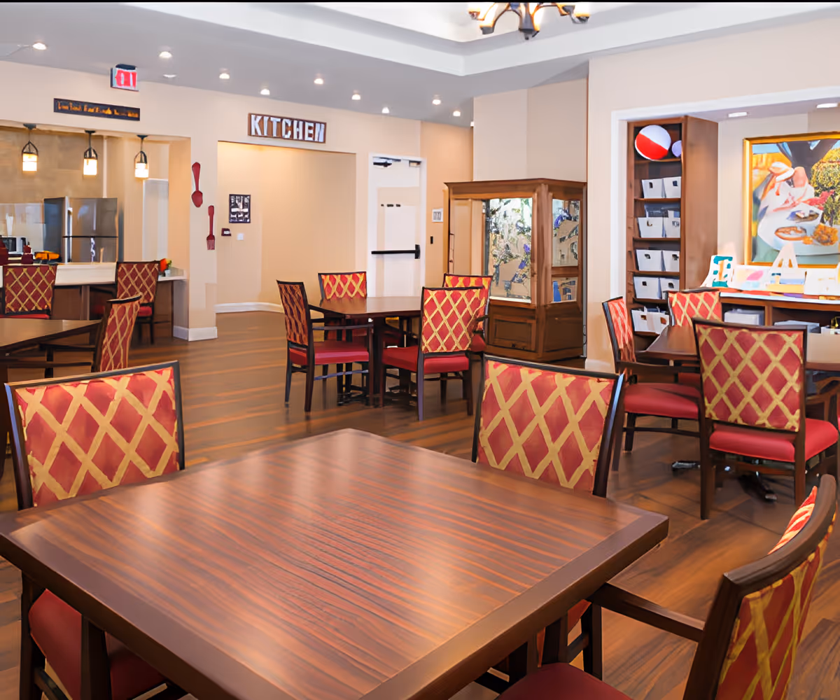 Dining room with multiple wooden tables and red patterned chairs, with a doorway labeled "KITCHEN" in the background.