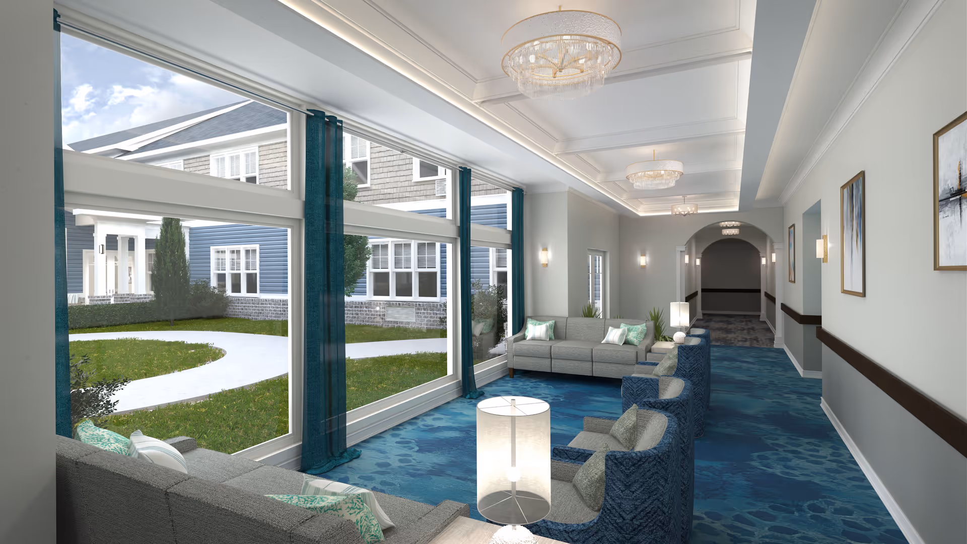 A bright and spacious lounge area with large windows overlooking a green courtyard. The room features comfortable gray and blue seating, decorative pillows, modern lamps, blue patterned carpet, and elegant chandeliers on the ceiling. The walls are adorned with framed artwork and wall sconces, and there is a hallway leading further into the building.