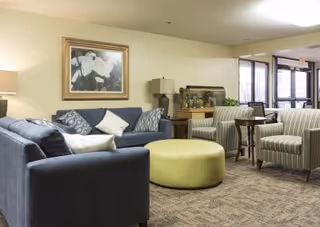 Comfortable lounge area with sofas, striped armchairs, a round ottoman, and an aquarium near glass doors.