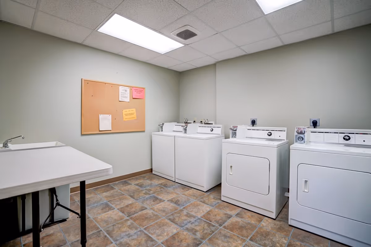 Community laundry room with washers and dryers, a folding table with sink, and a bulletin board on the wall.