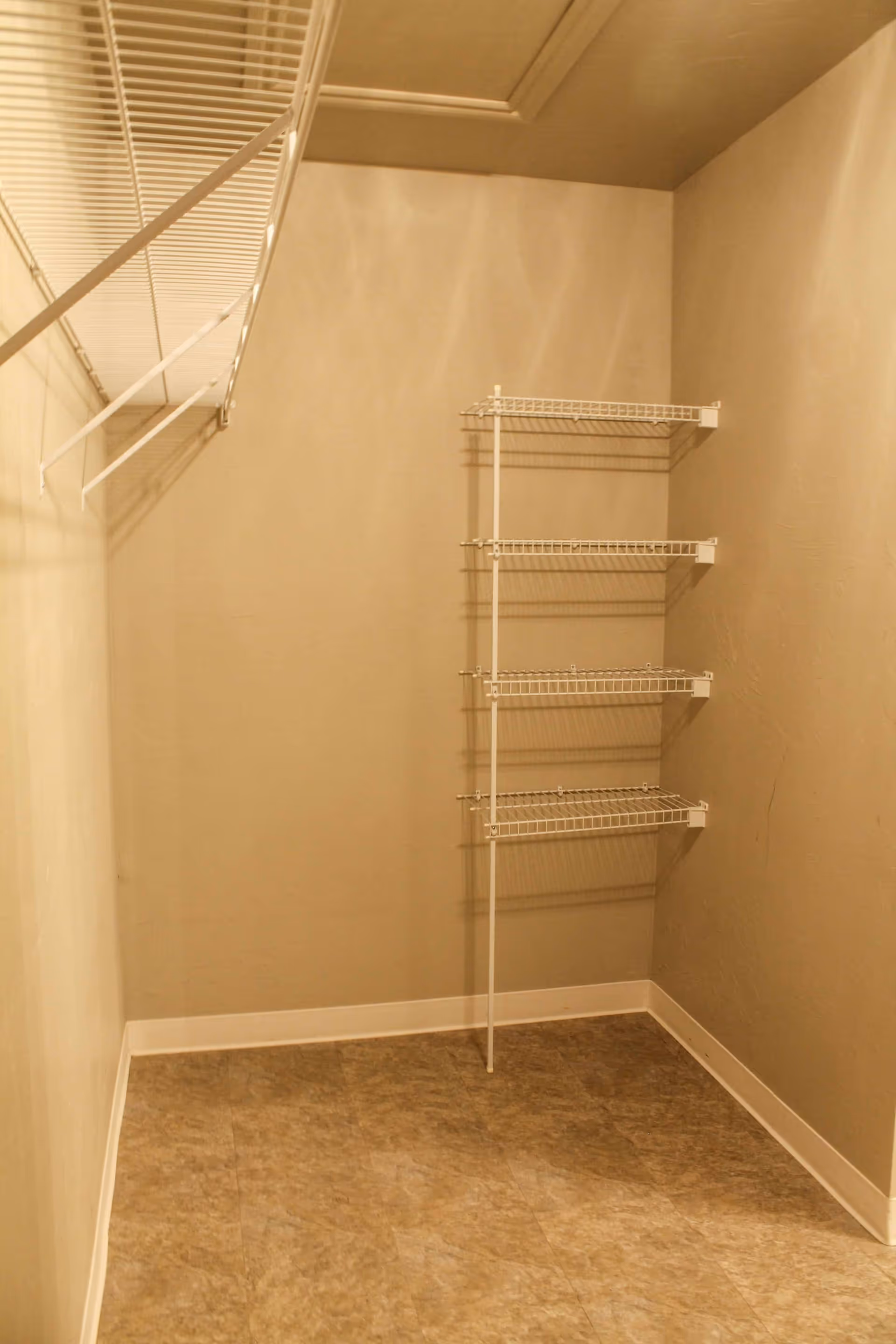 Empty walk-in closet with beige walls, tiled floor, and white wire shelving on the left wall and a set of four white wire shelves mounted on the right wall.