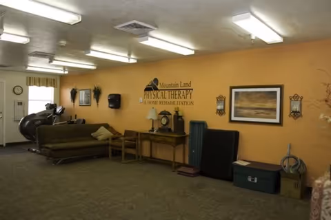 A spacious interior therapy room with couches, exercise equipment, and a wall sign reading 'Mountain Land Physical Therapy & Home Rehabilitation'.