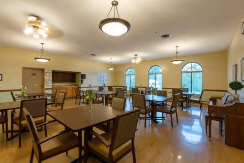 Spacious dining room with multiple tables and chairs, large arched windows, pendant lights, and a piano.