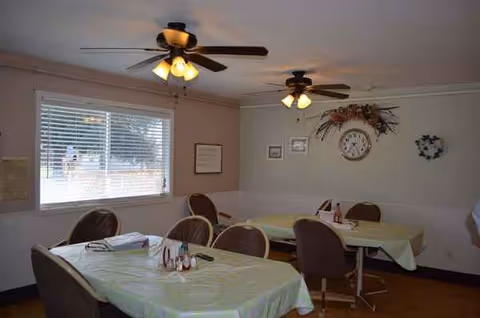 A dining room with two ceiling fans, window, and several covered tables.