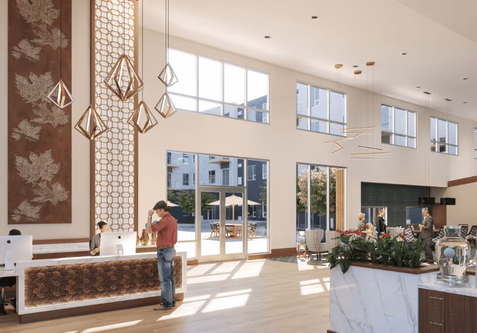 Bright two-story senior living lobby with large windows, a reception desk, geometric pendant lights, and seating where people are gathered.