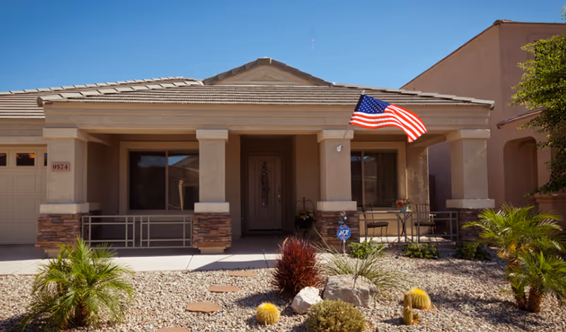 Front exterior of AZ Life Assisted Living Home with porch, flag, and desert landscaping.