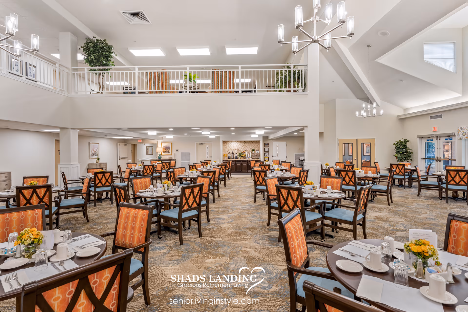 Spacious senior living dining room with multiple set tables and chairs under a high ceiling and balcony.