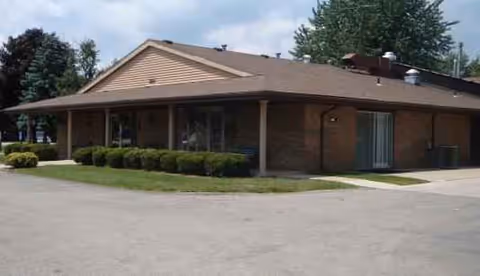 Single-story brick senior living facility with a covered entrance and trimmed shrubs.