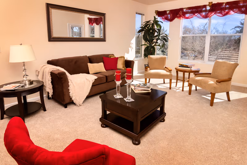 Bright furnished living room with a sofa, armchairs, coffee table and large windows letting in sunlight.