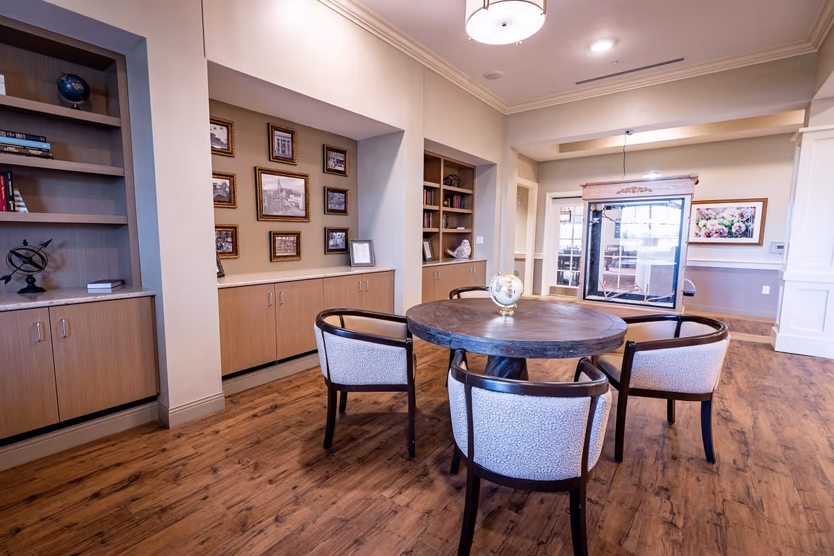 Communal lounge featuring a round wooden table with four upholstered chairs, built-in shelving, and framed photos on the wall.