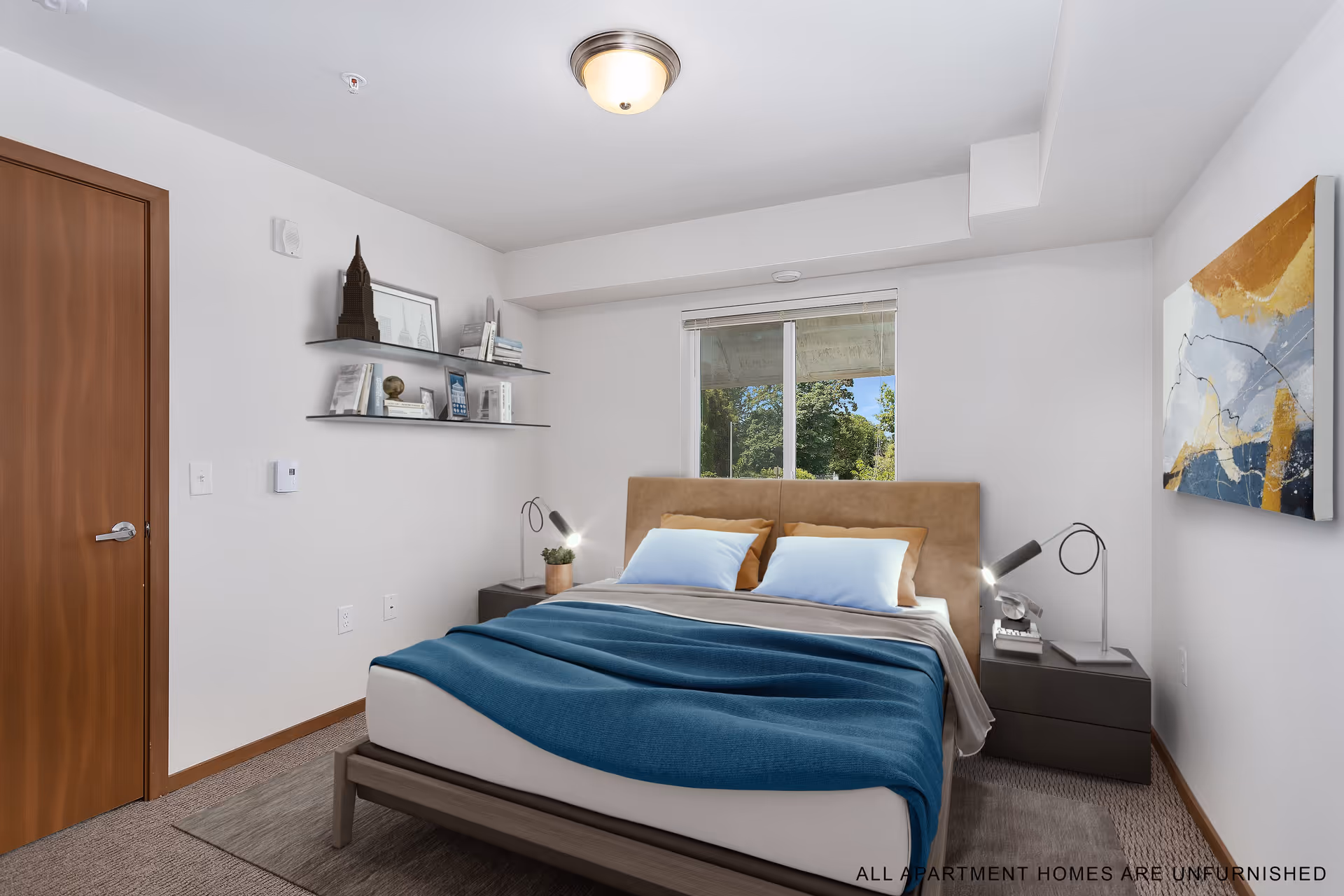 A bedroom with a large bed featuring a tan headboard, white and brown pillows, and a blue blanket. There are two dark nightstands on either side of the bed, each with a modern lamp. A window behind the bed shows greenery outside. On the left wall, there are two floating shelves with books and decorative items. A wooden door is on the left side of the room, and a colorful abstract painting hangs on the right wall. The room has white walls and carpeted flooring.