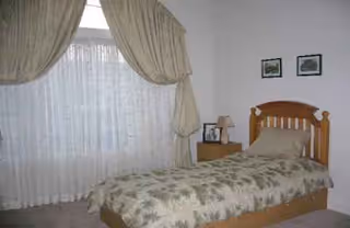 A wooden twin bed with a floral quilt, nightstand, and sheer draped curtains.