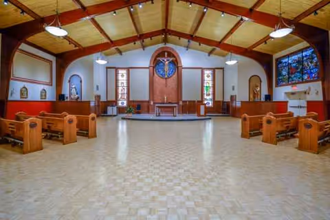 Interior view of a chapel-style room with wooden pews, stained glass, and an altar.