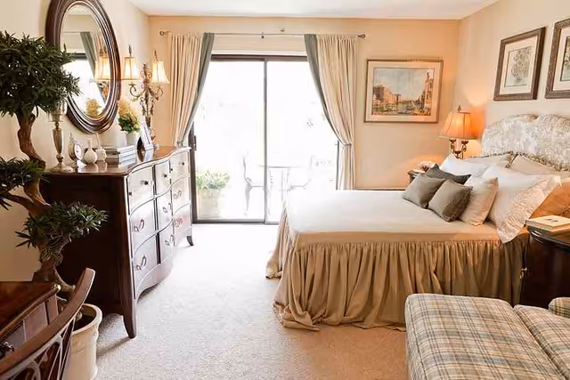 Bright, elegant bedroom with a bed, dresser, armchair, and sliding glass door leading to a balcony.
