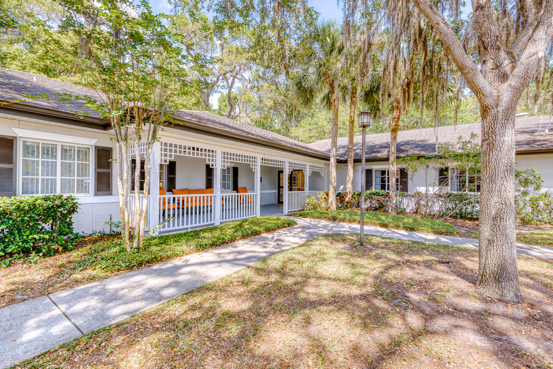 Front exterior of a ranch-style cottage with a covered porch, walkway, and surrounding trees and landscaping.