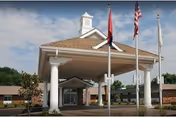 Covered porte-cochere entrance of a senior living building with white columns and three flagpoles.