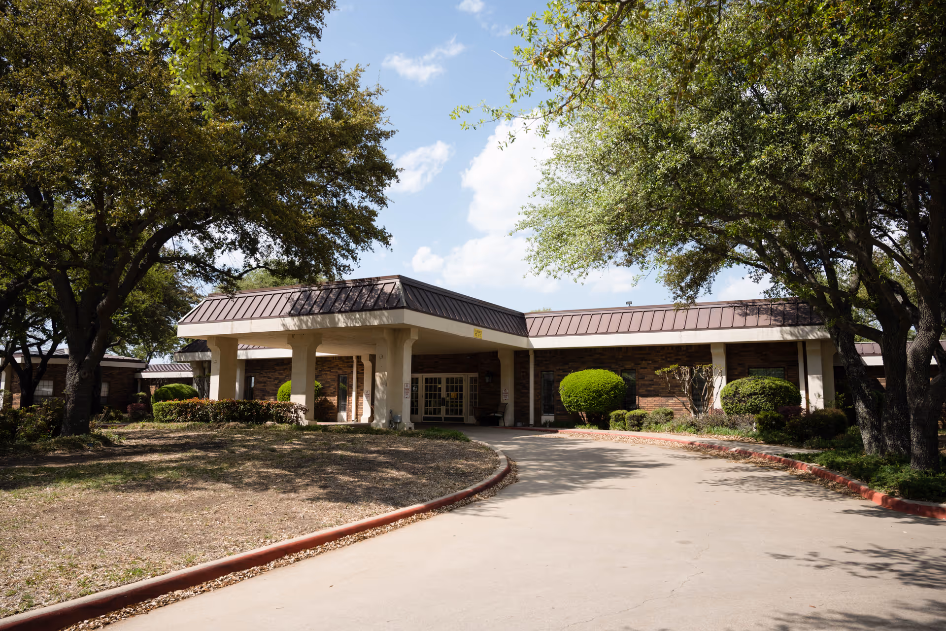 Front entrance of a single-story brick rehabilitation and healthcare center with a covered porte-cochère, circular driveway, and surrounding trees.