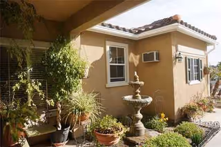 Exterior view of a beige senior living courtyard with potted plants and a fountain.