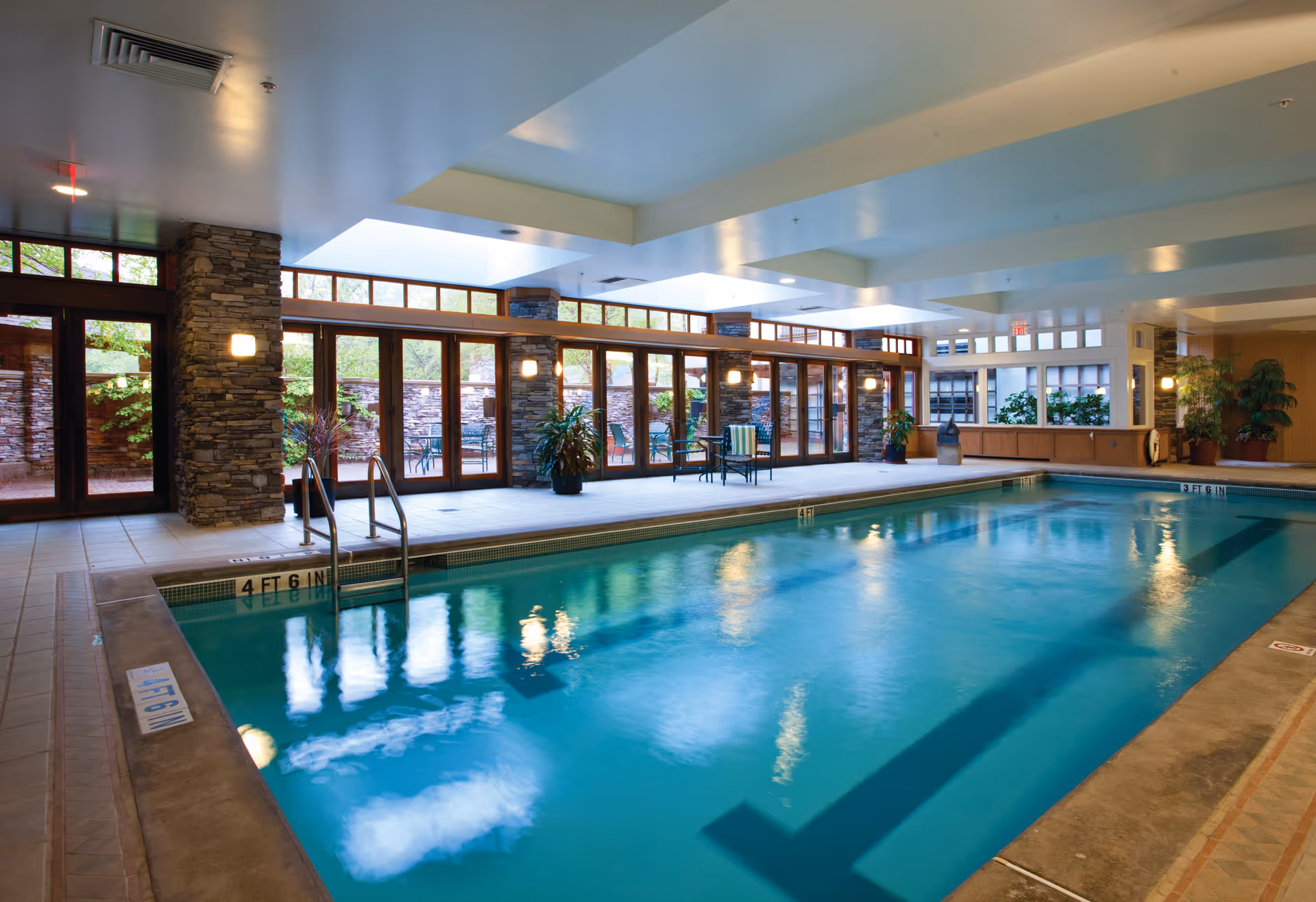 Indoor swimming pool with large windows, stone columns, and seating along the deck.