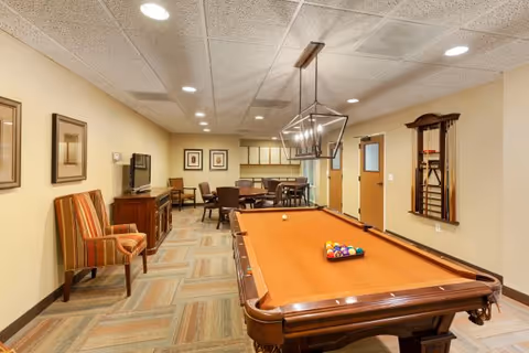 Interior common room with a pool table, seating area, TV, and dining table under recessed lighting.