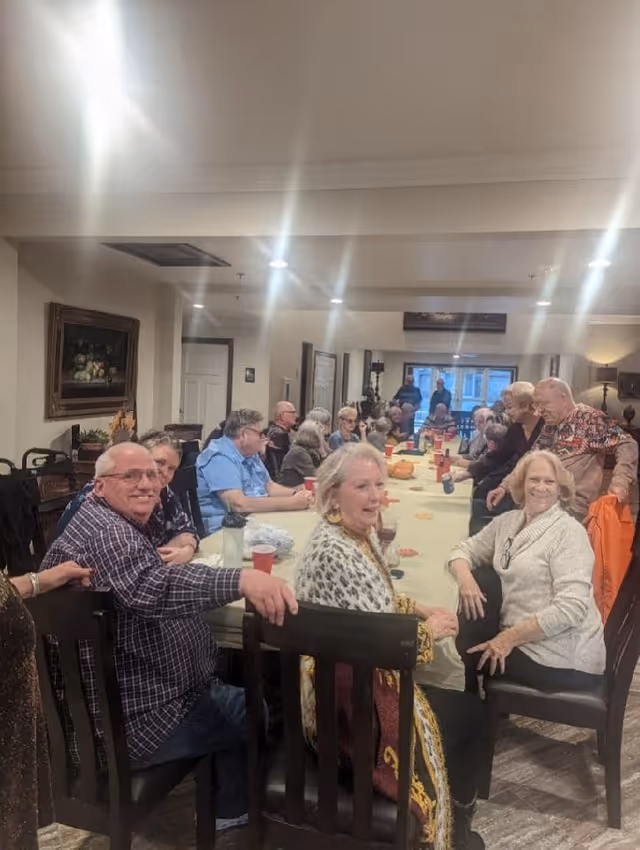 A large group of seniors seated around a long table in a communal dining room, smiling and socializing.