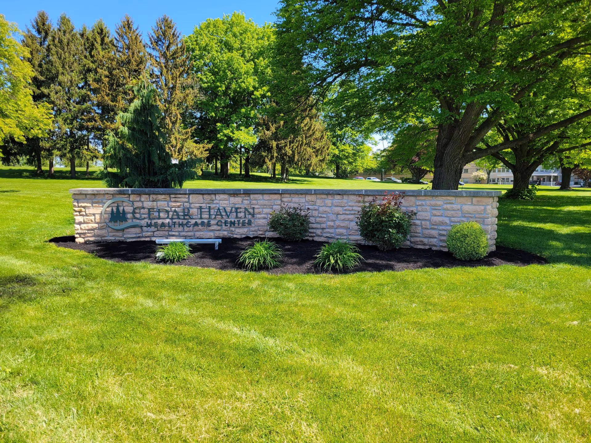Stone entrance sign reading "Cedar Haven Healthcare Center" on a manicured lawn with trees in the background.