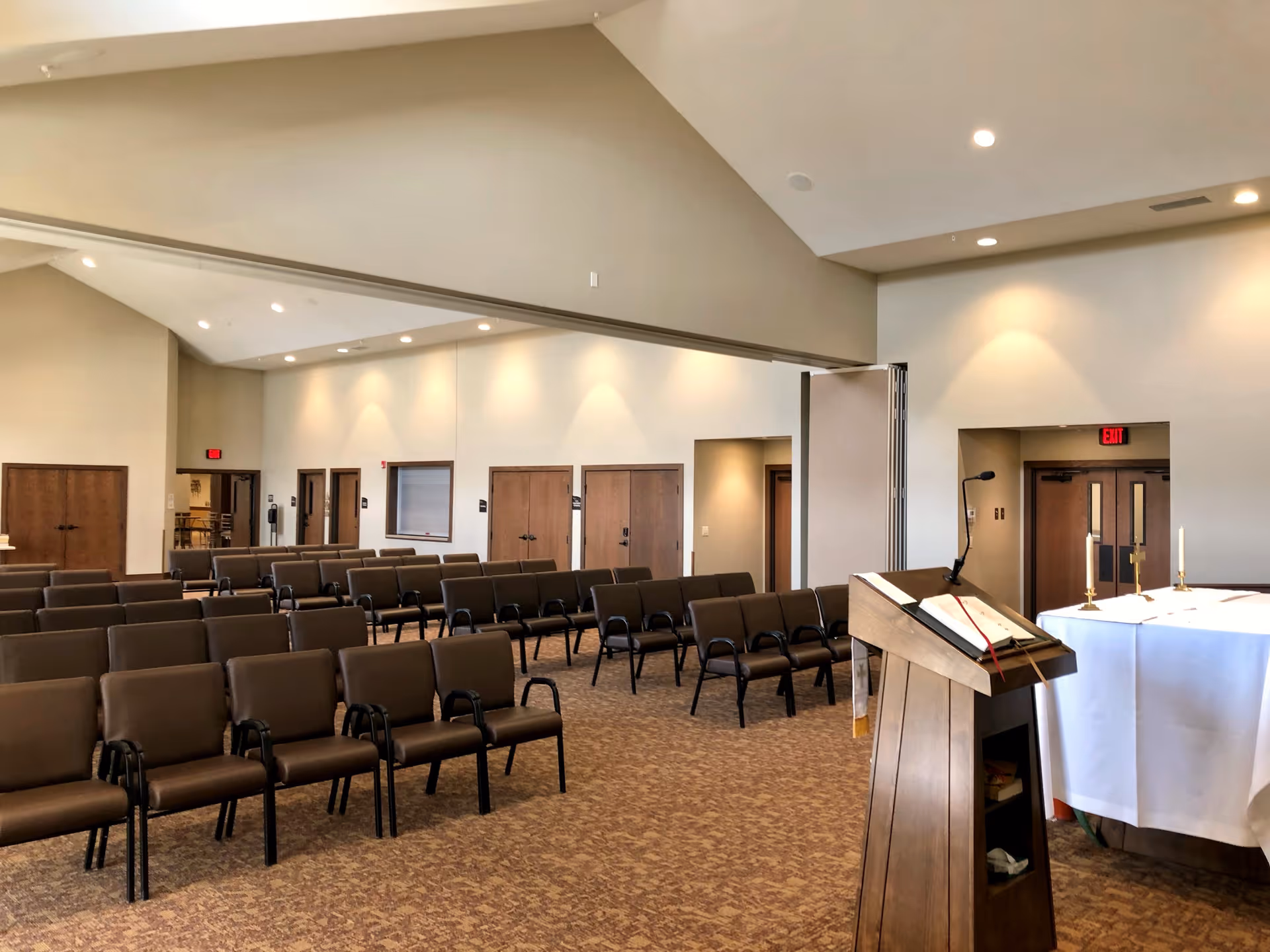Empty chapel-style meeting room with rows of brown chairs, a wooden lectern and a small altar at the front.