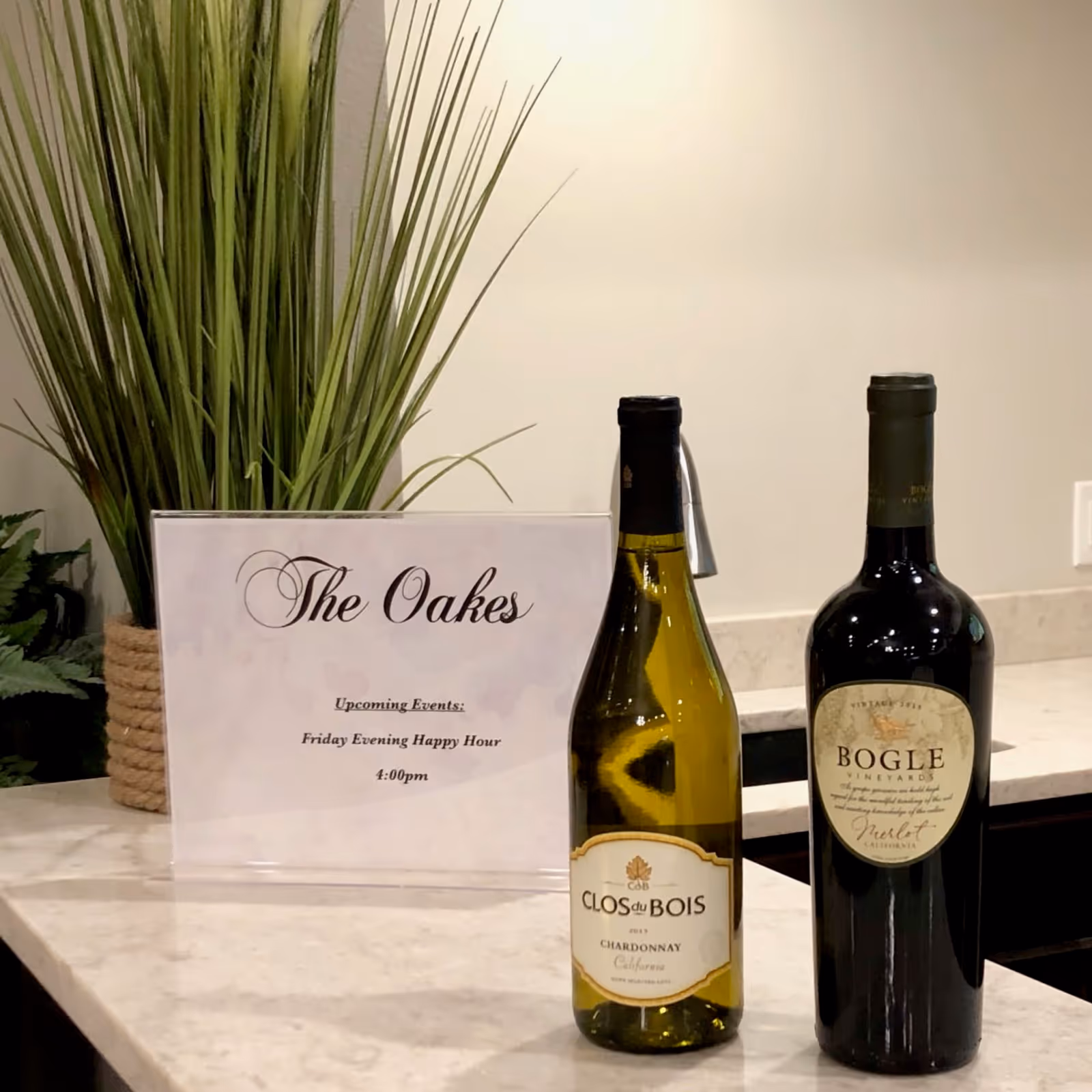 Two wine bottles on a marble countertop beside a small sign reading "The Oakes" and a potted plant in the background.