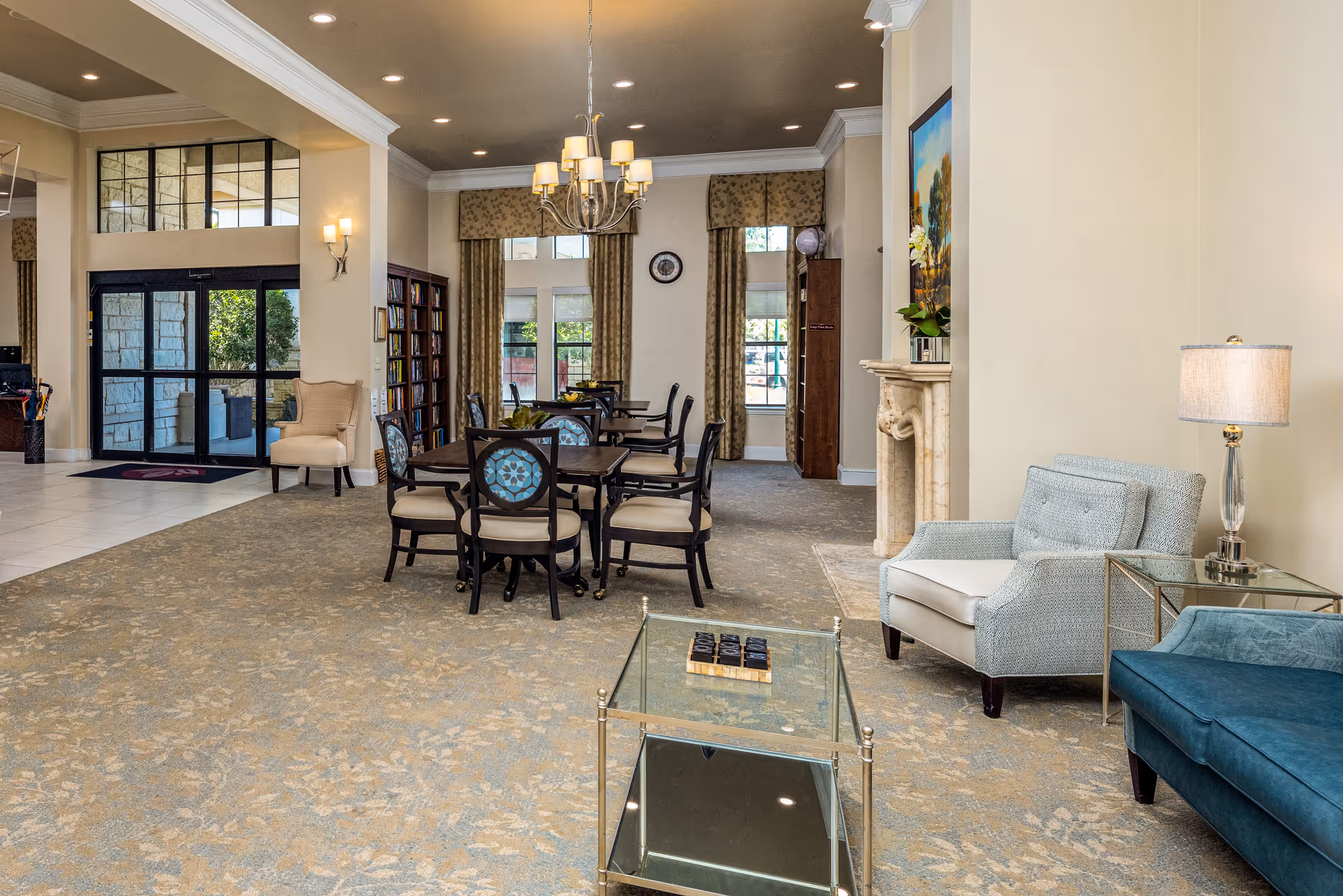 Well-lit senior living common room with dining tables, armchairs, and a glass entryway.